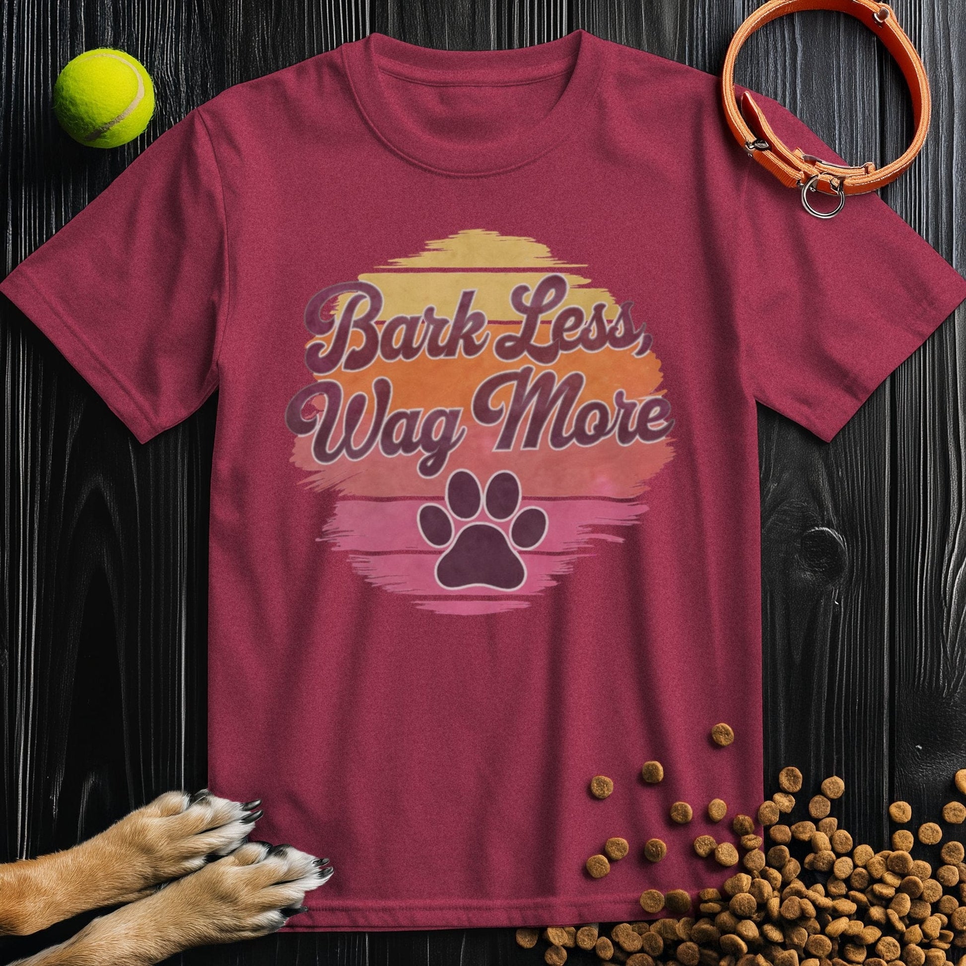 Maroon Bark Less, Wag More T-Shirt with colorful paw print and sunset design. Unisex cotton tee for dog lovers, regular fit.