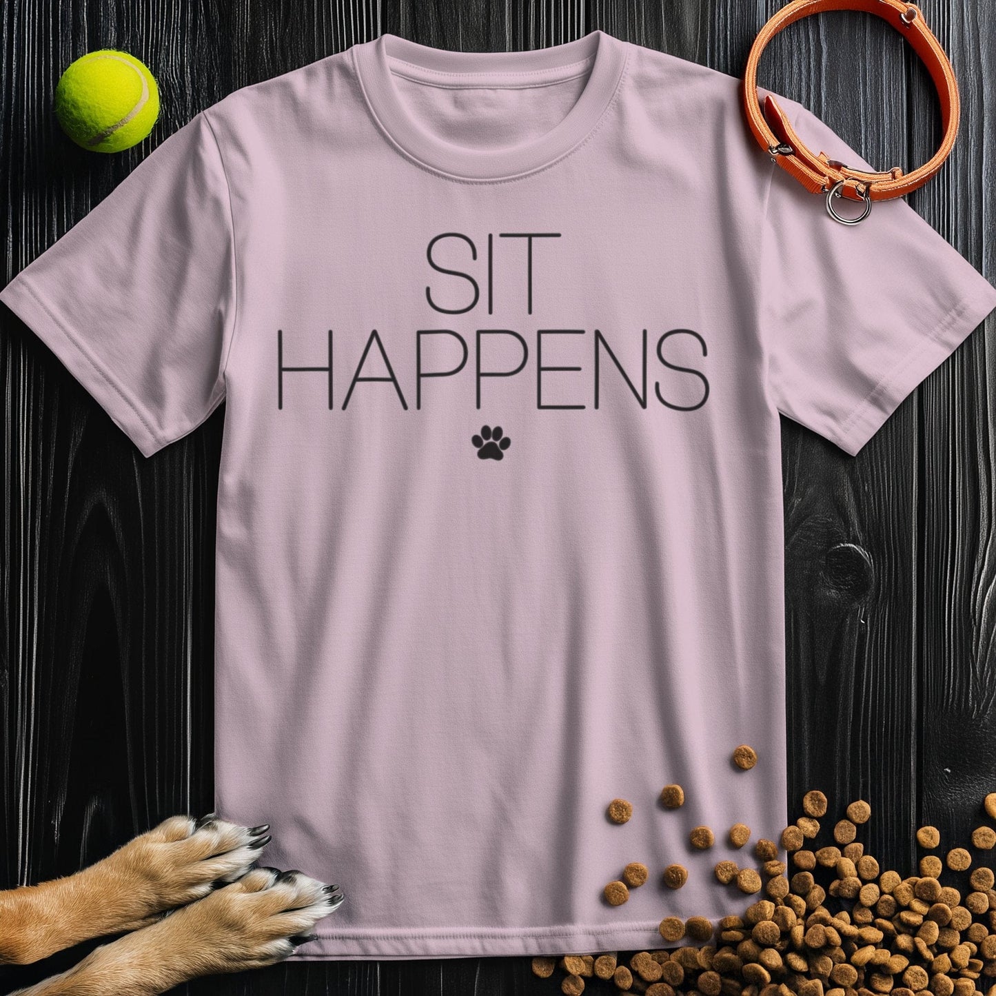 Light pink Sit Happens T-Shirt with black lettering and paw print, made from 100% cotton. A cute, ethical tee for dog lovers’ wardrobes.