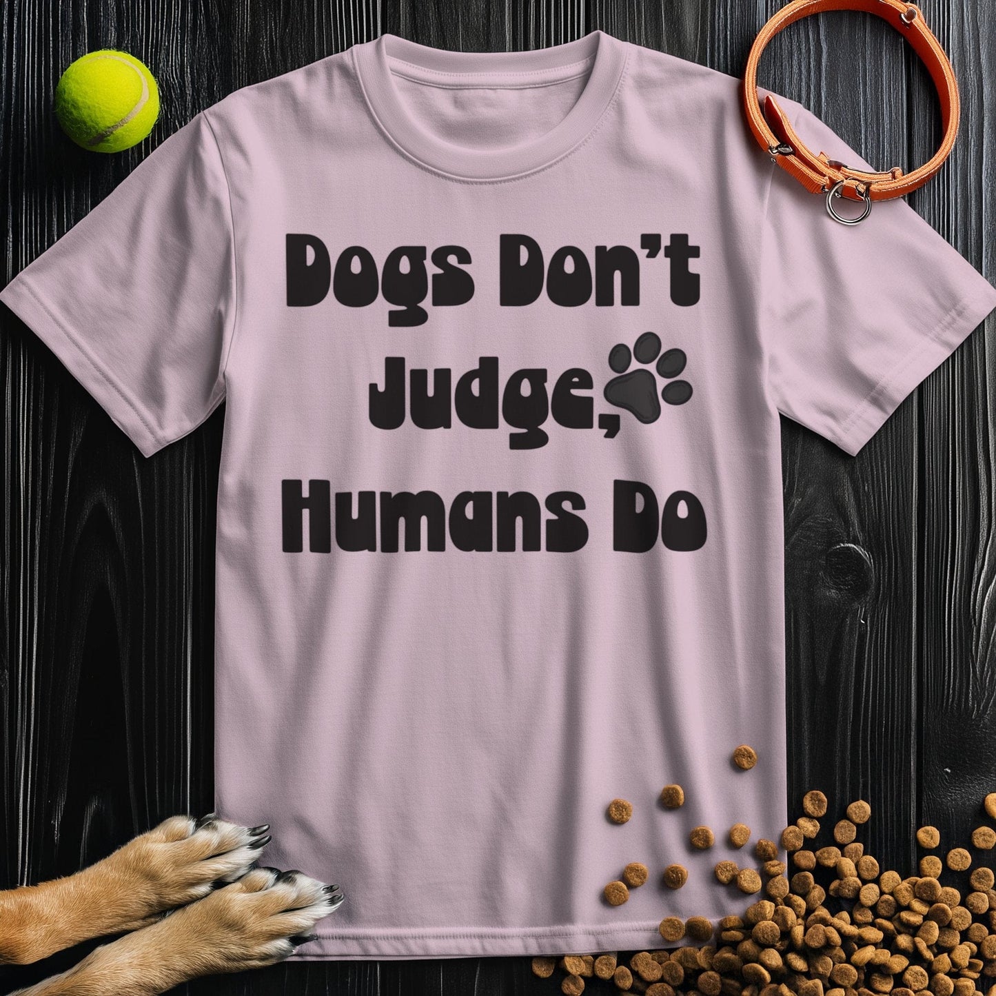 Light pink 'Dogs Don't Judge, Humans Do' t-shirt made from ethical cotton, featuring bold black lettering and a paw print for pet enthusiasts.